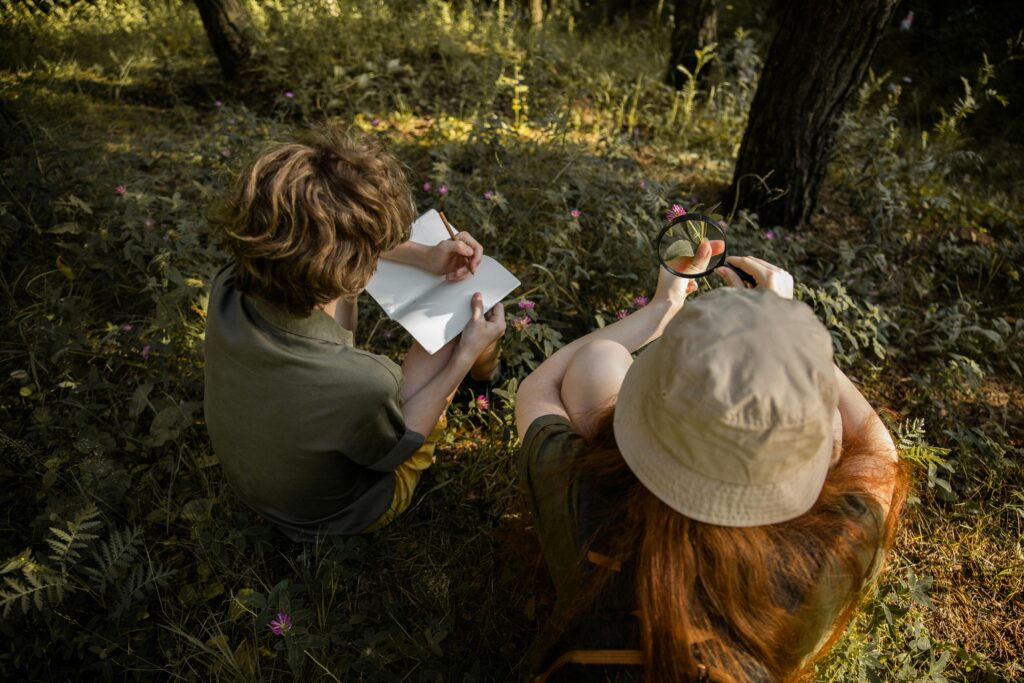 pexels photo 5036722 5036722 Two kids explore a forest, observing nature with a sketchbook and magnifying glass.